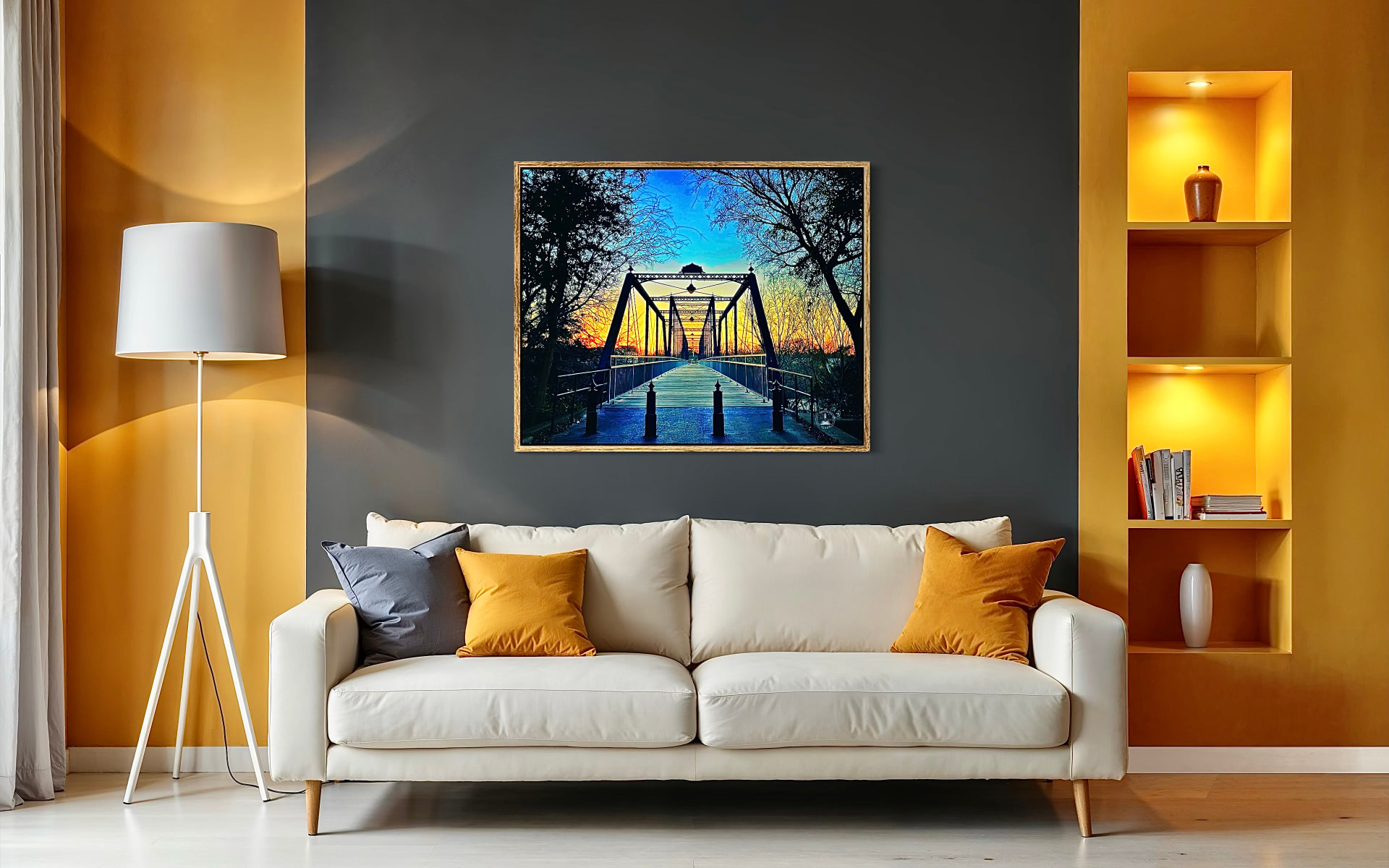Vivid sunset truss bridge photograph framed above a cream sofa beside warm gold lighted alcoves